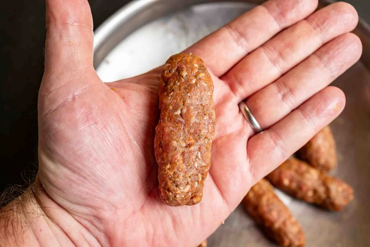 Hände formen Cevapcici aus gewürztem Hackfleisch